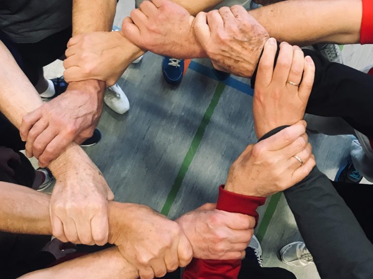 Das Bild zeigt Männer im Kreis, die sich an den Armen gegenseitig halten.